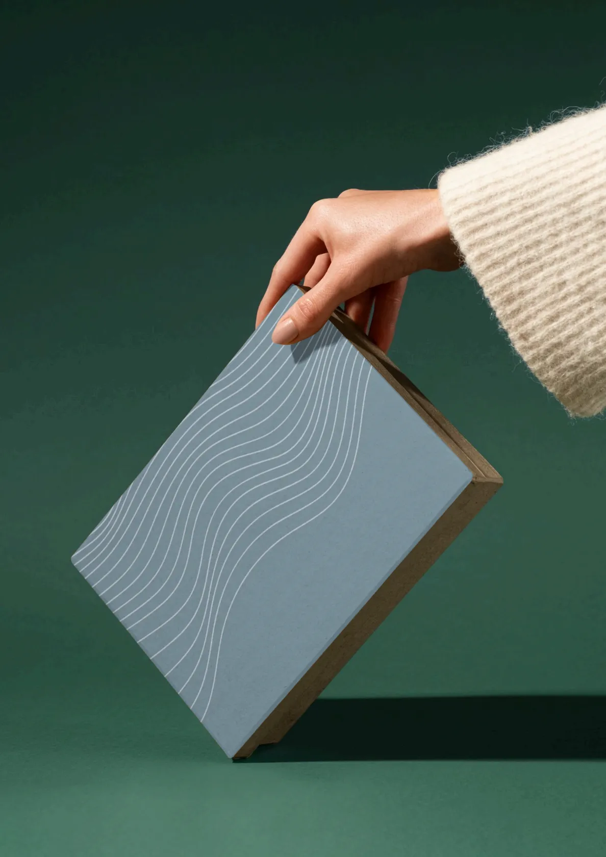 Minimal branded packaging held over a green backdrop